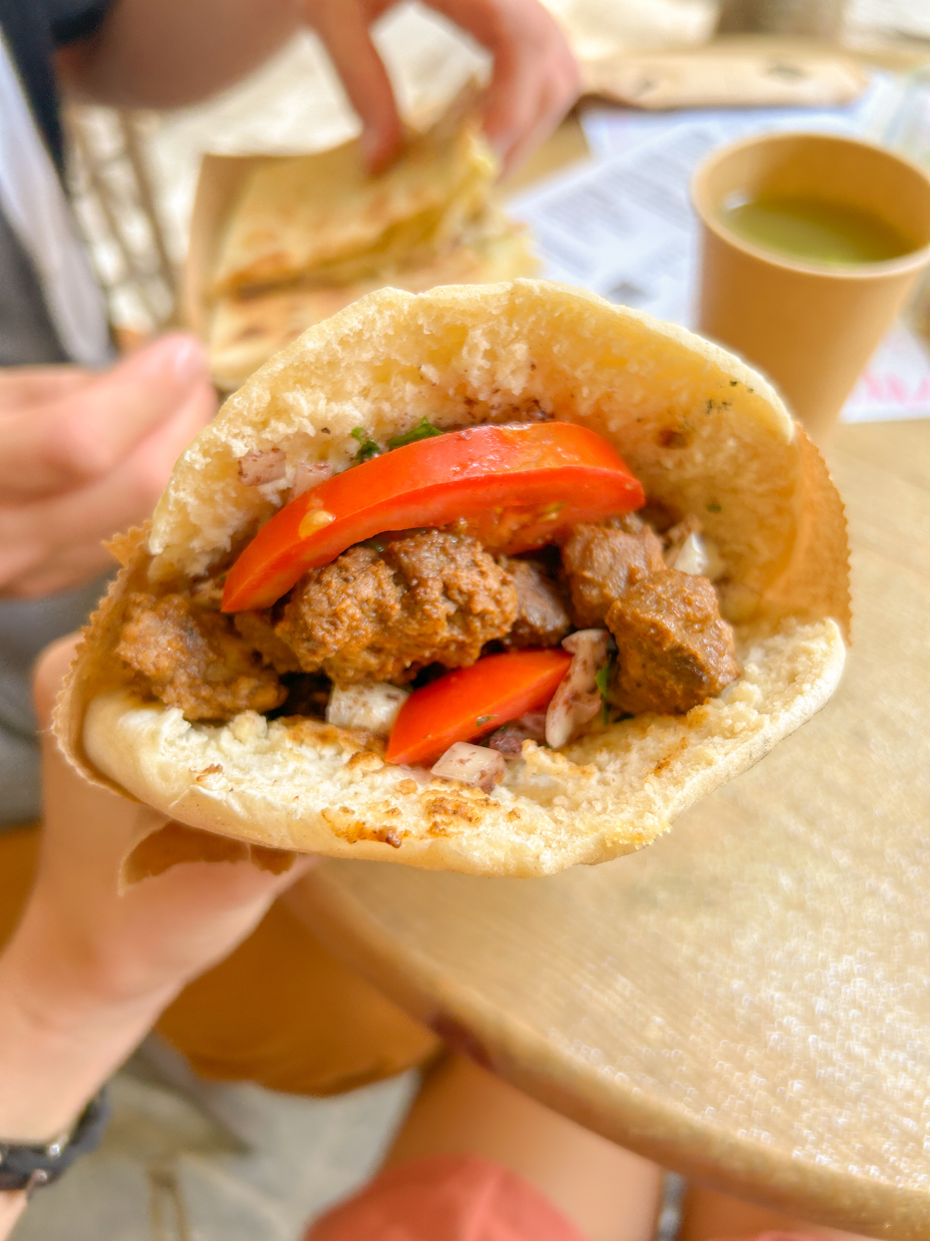 Pita bread split in half filled with brown lentil meatballs and tomatoes.
