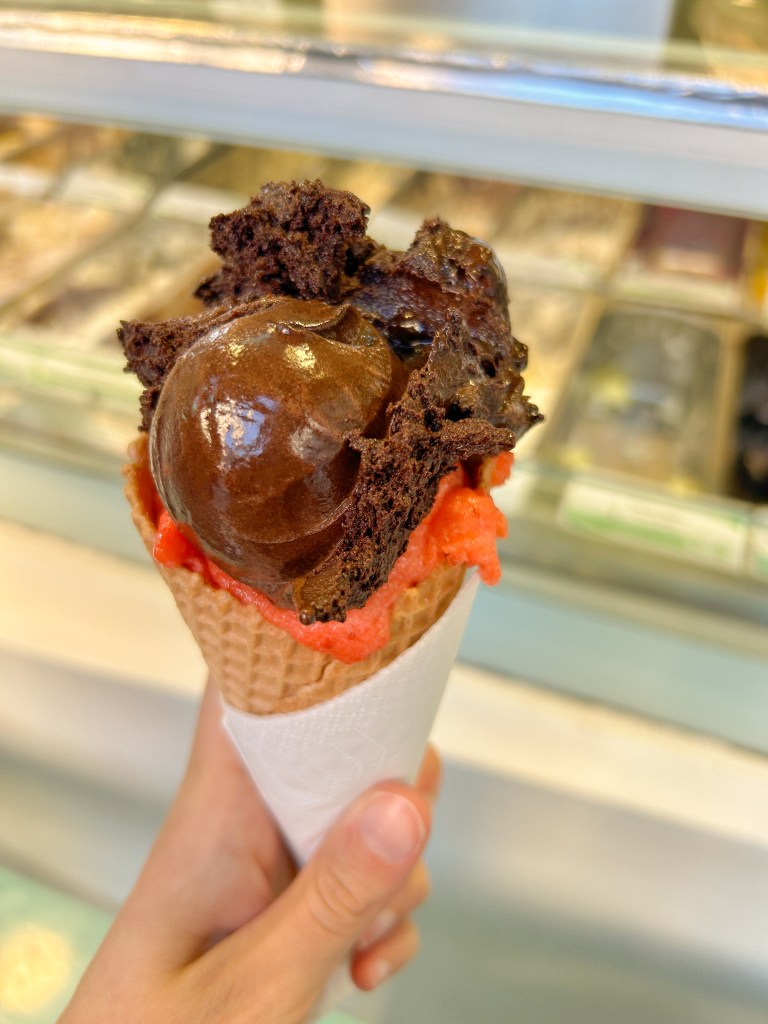 Ice cream cone with one scoop of red strawberry ice cream on the bottom, and one scoop of chocolate ice cream on the top.