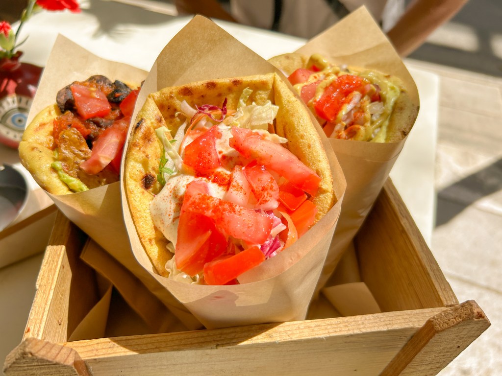 Three gyro wraps placed upright in a wooden box. Features tomatoes, lettuce, sauce, mushroom meat, and pita bread.