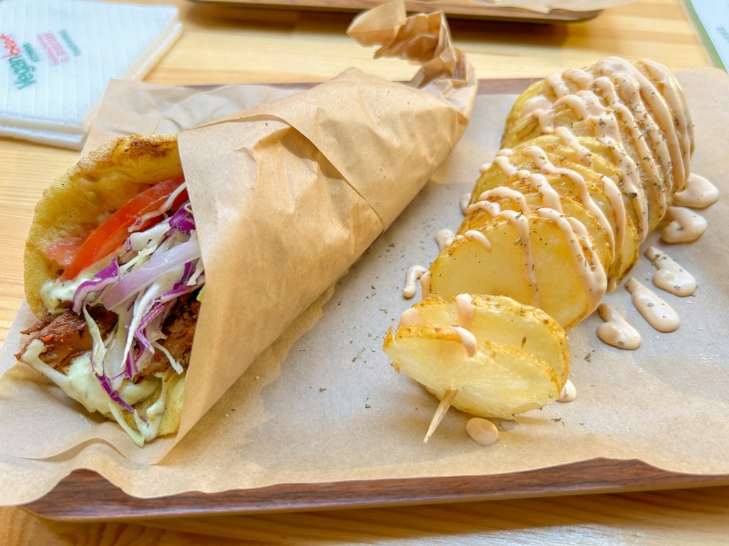 Mushroom gyro wrap with tomatoes, cabbage, onions, and sauce. On the side there is a spiralized potato with sauce drizzled on top.