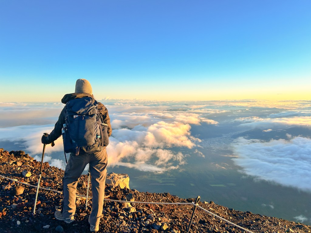 Person in hiking gear and backpack looks at the sky from the summit of the mountain.